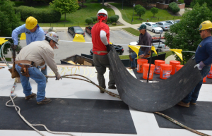 Asphaltic core boards are very flexible and will conform to irregular surfaces and offsets without fracture. Here crews work to install the cover board in bead-foam adhesive in preparation for the three-ply modified bitumen roof cover. PHOTO: Clark Roofing