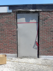 PHOTO 6: Even the existing door was low to the existing roofing at SD 113 Deerfield High School. Here the door frame has been removed; the door has been placed for interior protection.