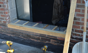 PHOTO 8: Here the door sill is being raised with wood blocking at SD 113 Deerfield High School. Because the brick was offset with the interior CMU, two layers of wood were installed at the exterior and one layer of shimmed wood will be installed on the interior. The interior sill will be covered with membrane, followed by prefinished metal and door sill.