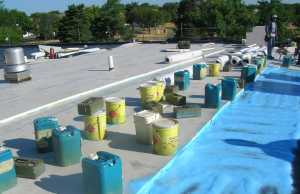 PHOTO 7: The blue spray-foam adhesive applied to the existing EPDM is allowed to rise prior to setting the new double-coated, fiberglass-faced, mold-resistant insulation. To ensure positive embedment into the adhesive and bonding, the insulation is weighted in place. The author’s spec requires 5- to 35-pound weights per board for a minimum of five minutes.