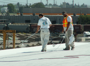 A spray-applied reflective coating is being installed over an existing granule-surfaced asphaltic roof.  PHOTO: GAF, courtesy of the Roof Coatings Manufacturers Association